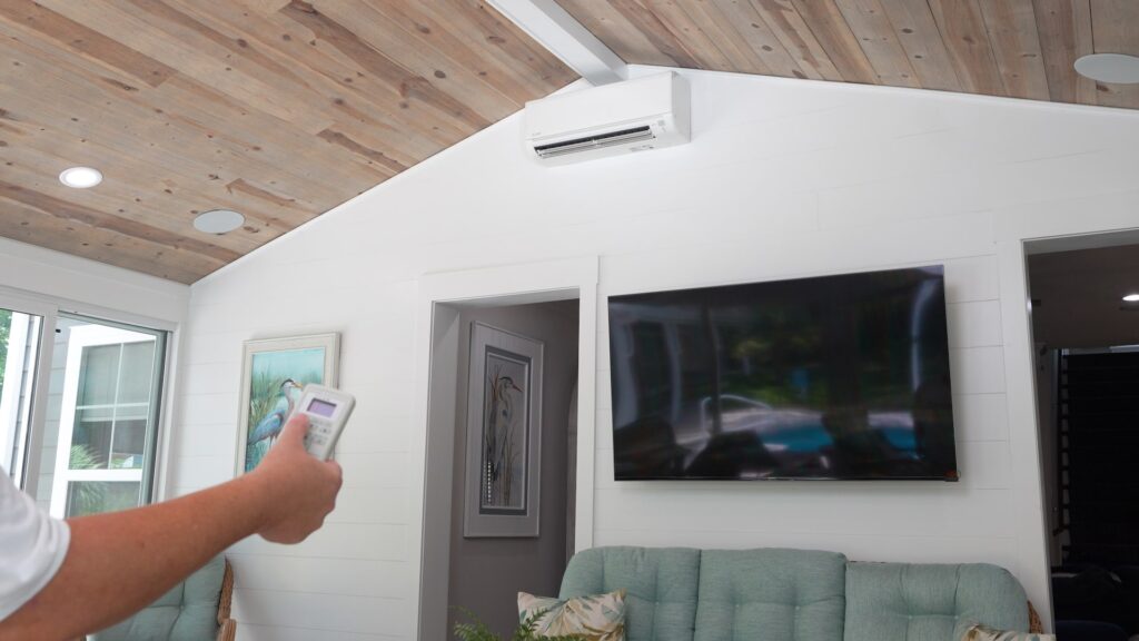 A persons hand holds a remote to a minisplit system in a sunroom - ECCO Sunroom & Awning