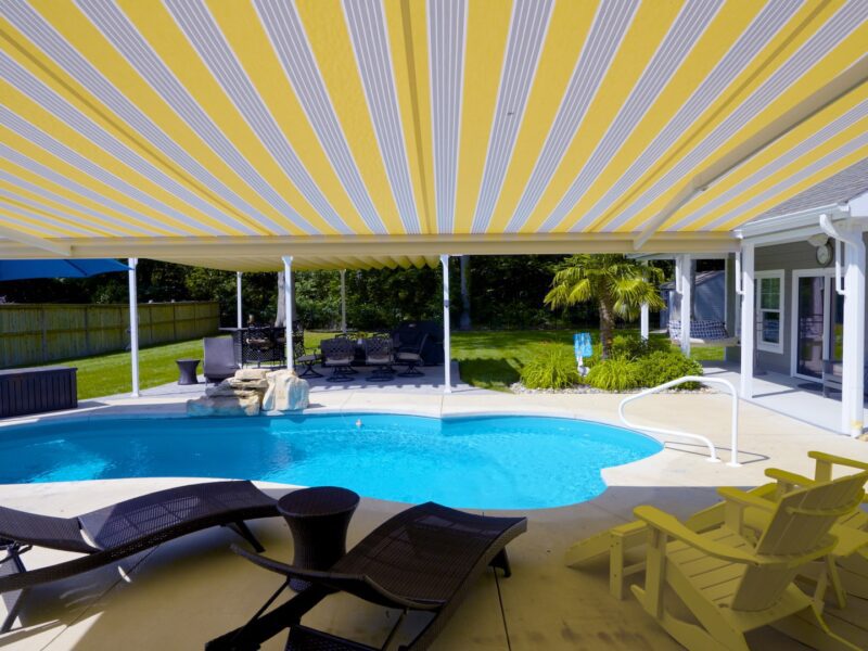 Lounge chairs by pool under a retractable motorized awning - ECCO Sunroom & Awning | Benefits of Retractable Awnings