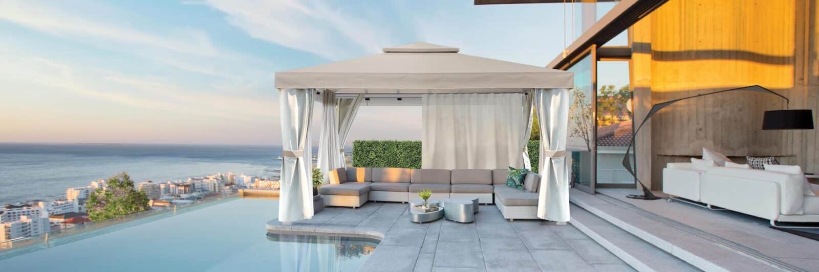 Infinity pool and patio of modern house. Open air cabana with curtains and privacy curtains covers outdoor couch